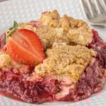 Close-up of strawberry cream cheese dump cake with golden crumb topping and juicy strawberry filling on a white plate