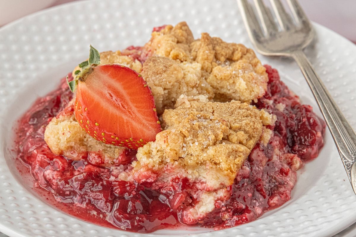 Close-up of strawberry cream cheese dump cake with golden crumb topping and juicy strawberry filling on a white plate