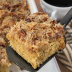 Old-fashioned oatmeal cake with coconut pecan topping on a spatula, with a cup of coffee in the background and text reading “Vanished. No witnesses.”