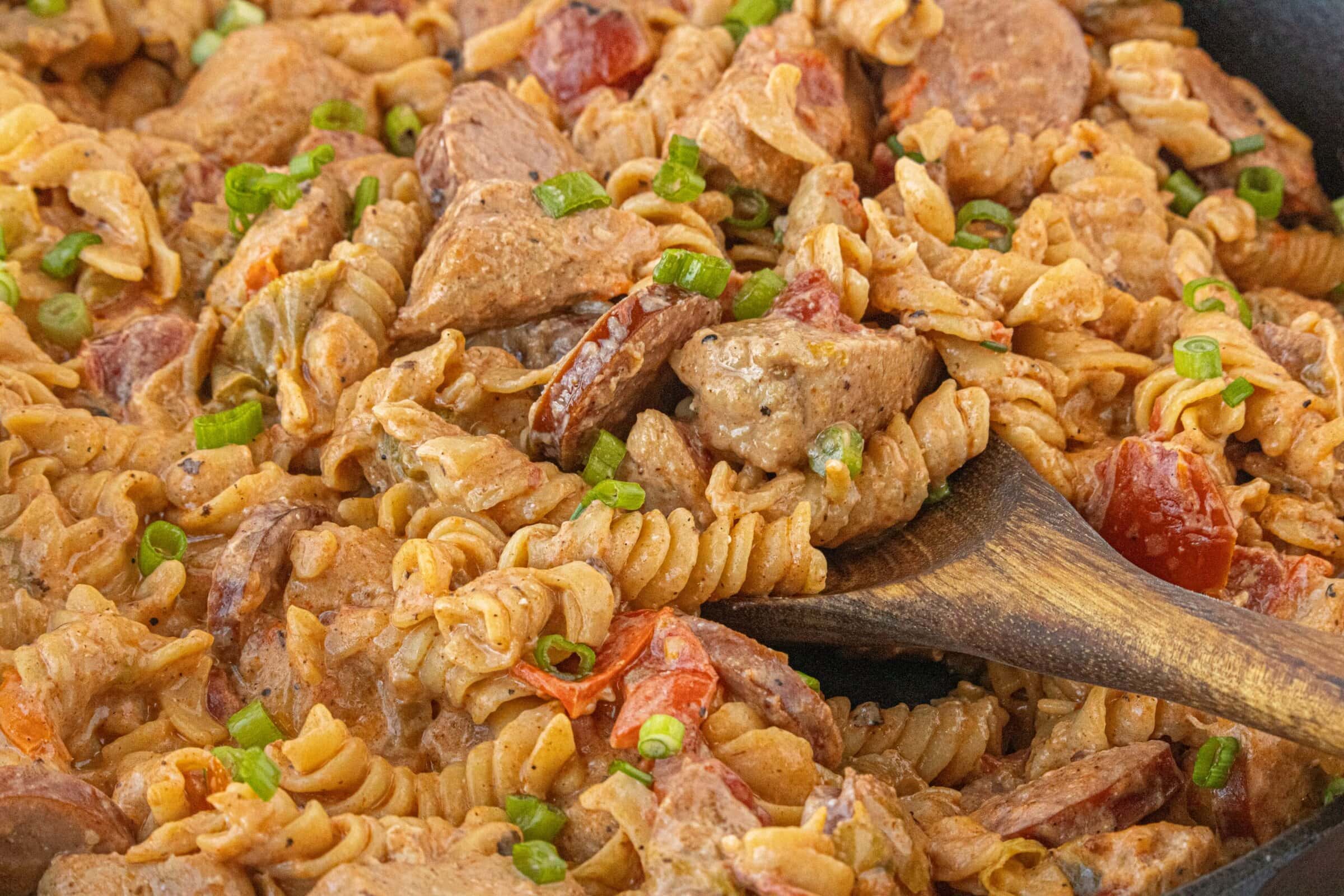Close up Cajun chicken and sausage pasta being stirred showing creamy Cajun sauce and rotini pasta