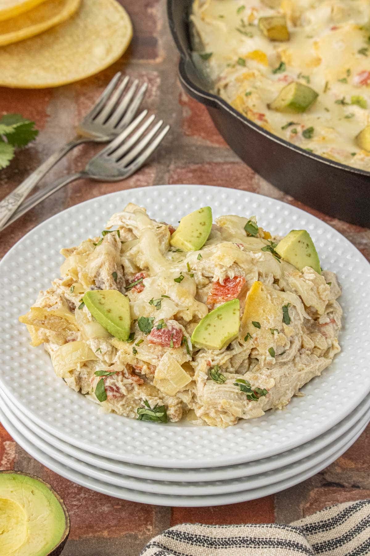 creamy skillet enchiladas suizas with shredded chicken, melted monterey jack cheese, avocado, and cilantro on a white plate