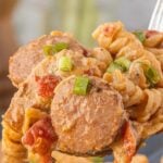 Spoonful of creamy Cajun chicken and sausage pasta with smoked sausage, chicken, fire roasted tomatoes, and green onions with text overlay about restaurant vibes and 30 minute dinner