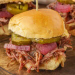 Close-up of a barbecue brisket slider topped with pickles and pickled onions on a soft slider bun.