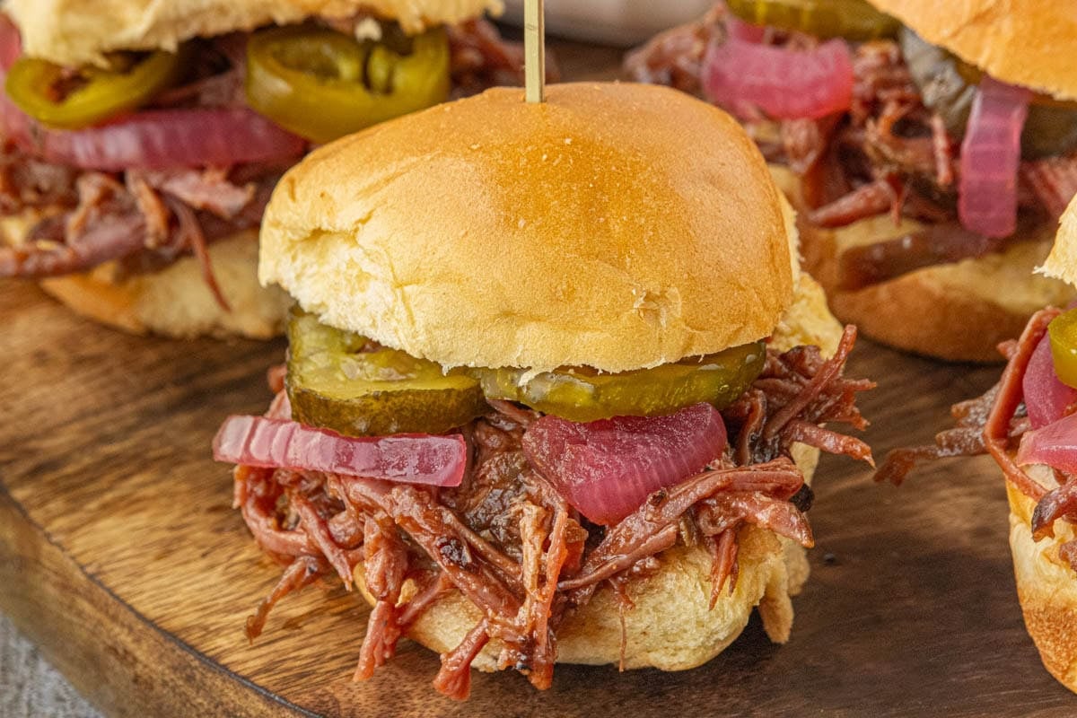 Close-up of a barbecue brisket slider topped with pickles and pickled onions on a soft slider bun.