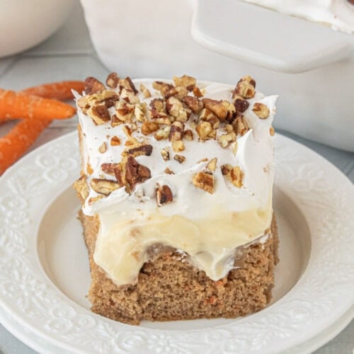 Carrot cake poke cake slice with thick creamy pudding filling and whipped topping, sprinkled with chopped pecans.