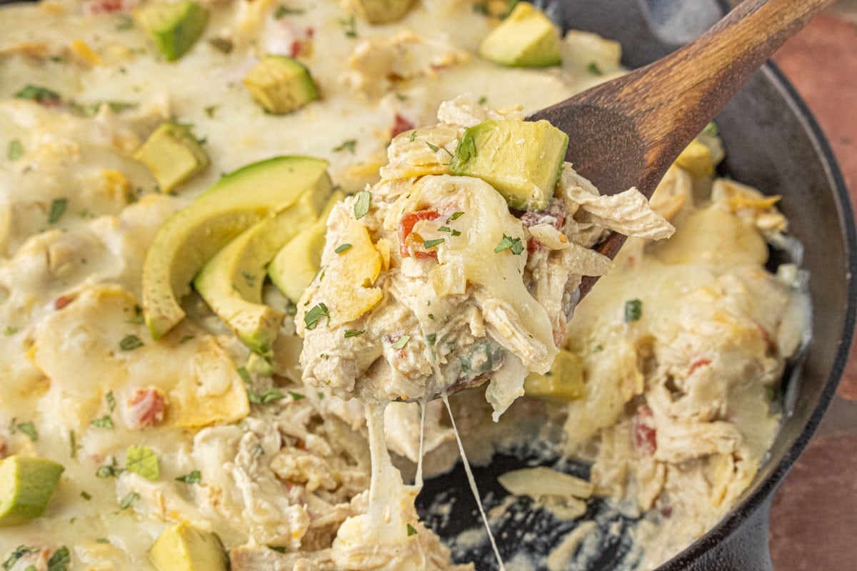 baked skillet enchiladas suizas topped with melted cheese and fresh avocado in cast iron pan
