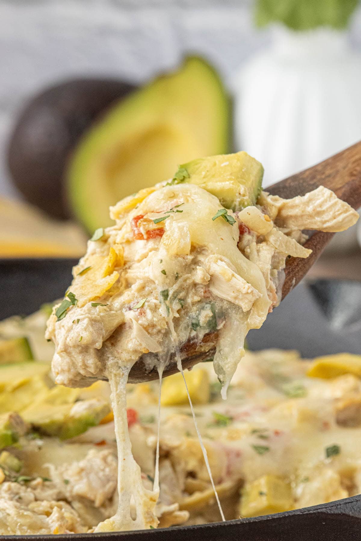 skillet enchiladas suizas being served with melted cheese, shredded chicken, and avocado slices