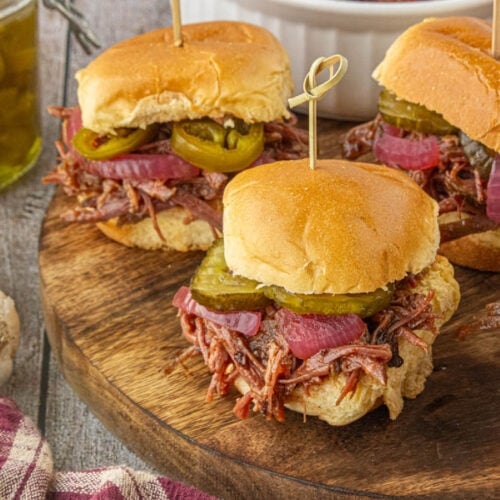 Slow cooker brisket sliders topped with pickles and pickled onions served on a wooden board.