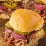 Slow cooker brisket sliders piled with tender shredded barbecue brisket, pickles, and pickled onions on soft slider buns.