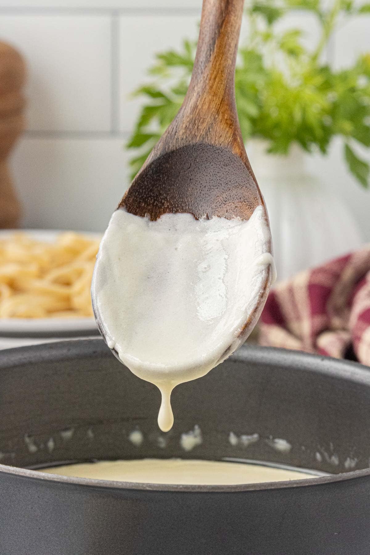 Thick 3 ingredient Alfredo sauce dripping from wooden spoon over skillet