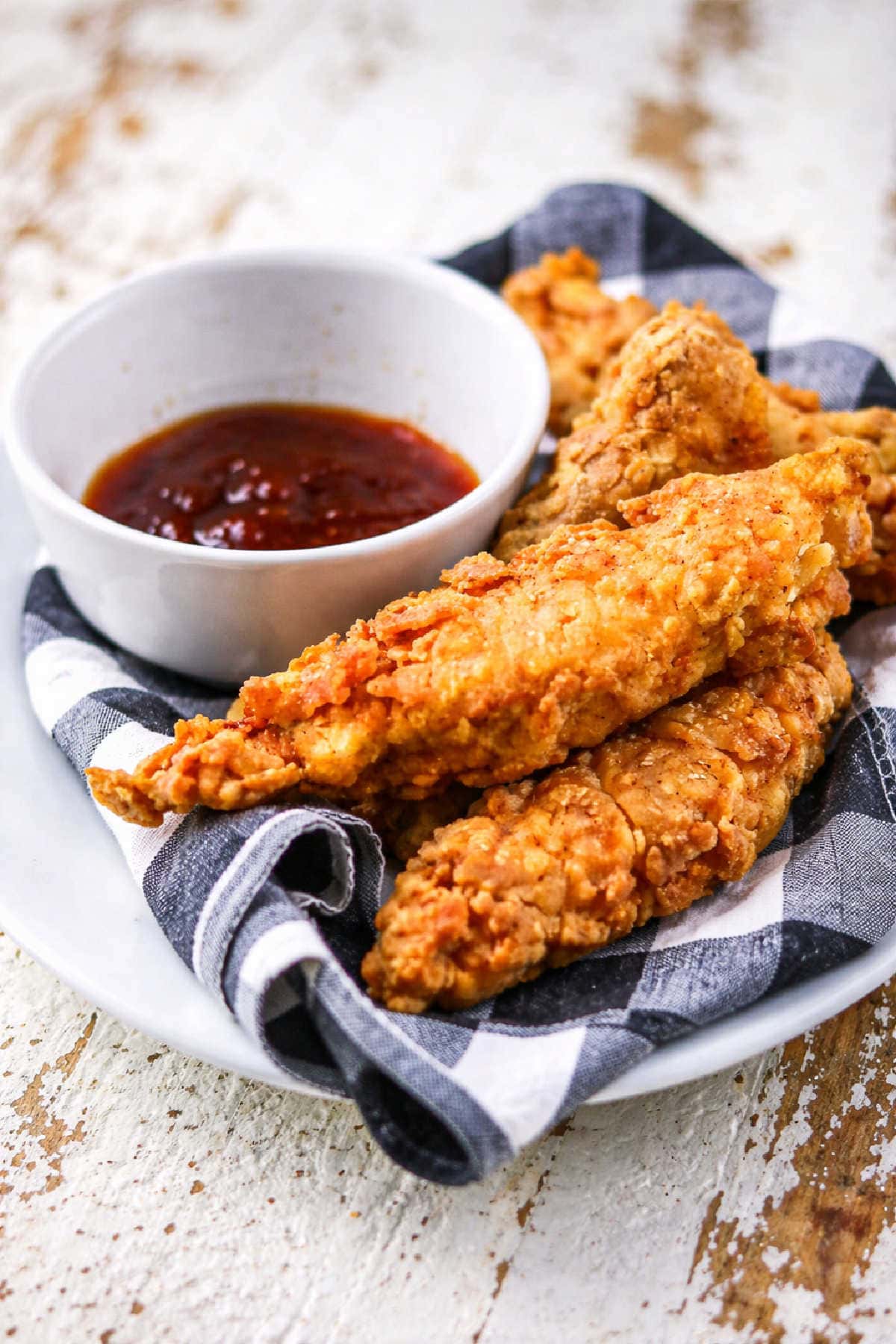Pieces of copycat Popeye's chicken tenders next to bbq sauce on a plate.