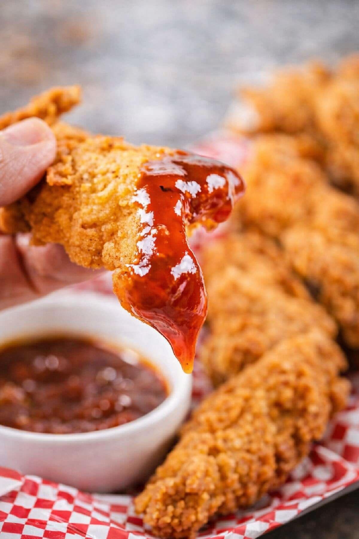 Copycat popeye's chicken tenders dipped in bbq sauce.