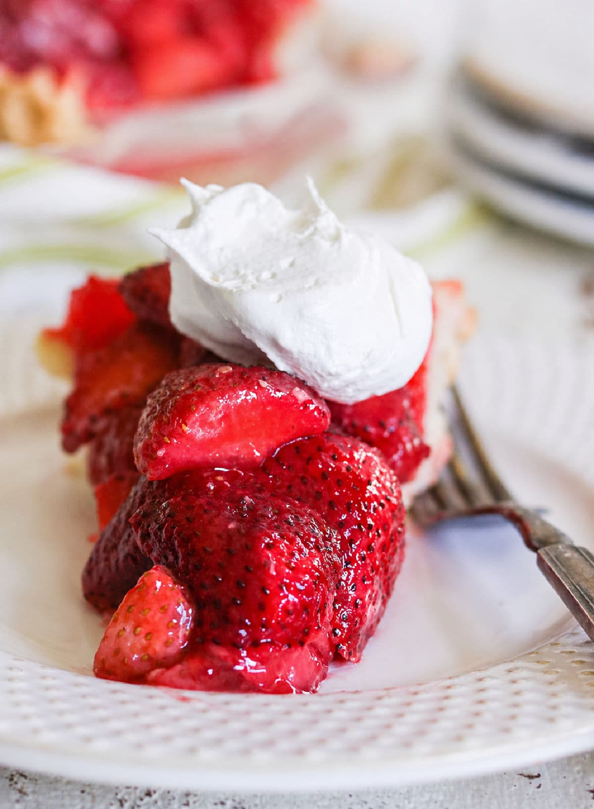 A slice of copycat Shoney's strawberry pie on a white plate with whipped cream on top.