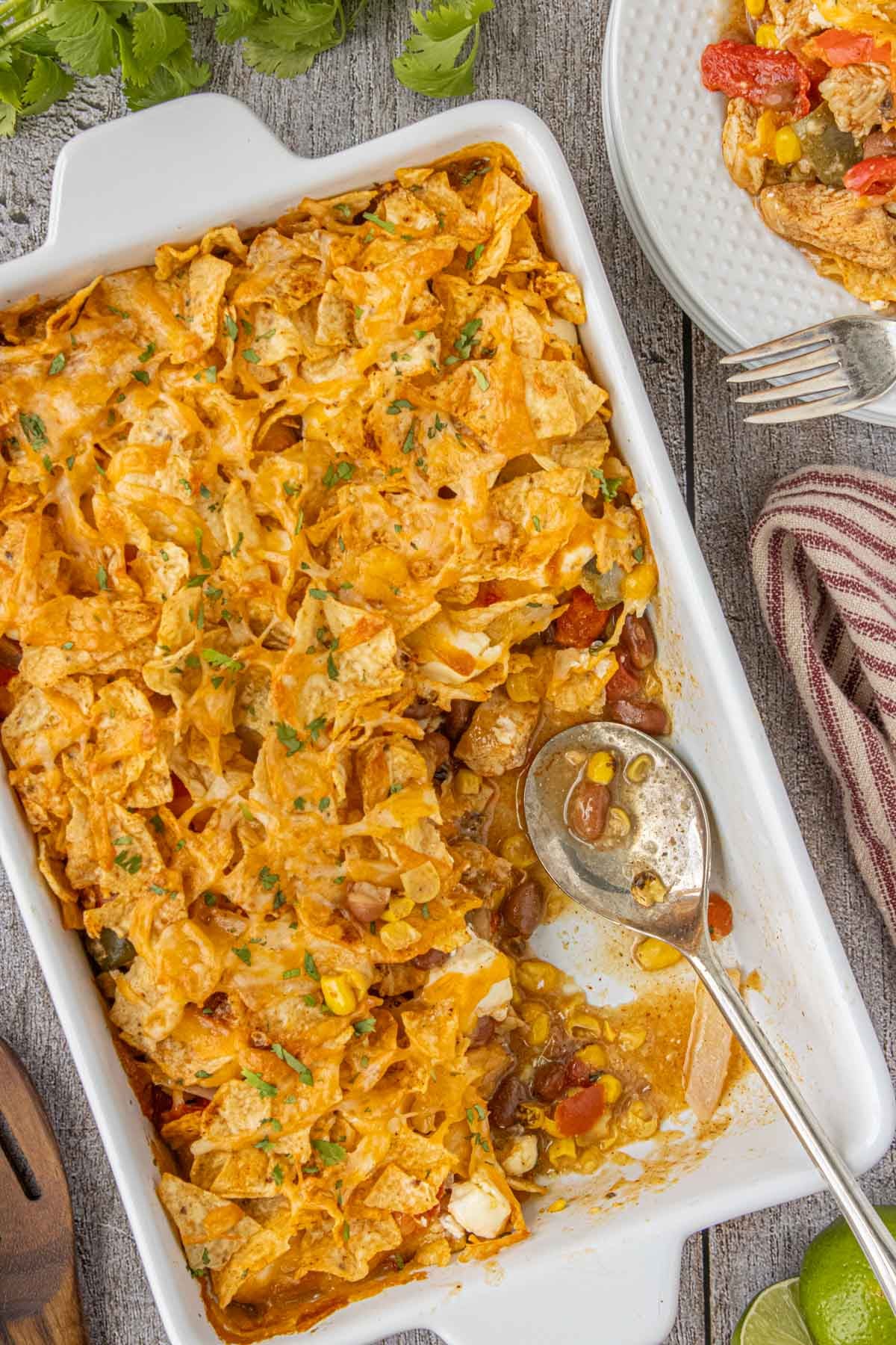 Baked 7 layer Tex-Mex chicken casserole topped with crunchy tortilla chips and melted cheese in a white casserole dish with a serving removed.