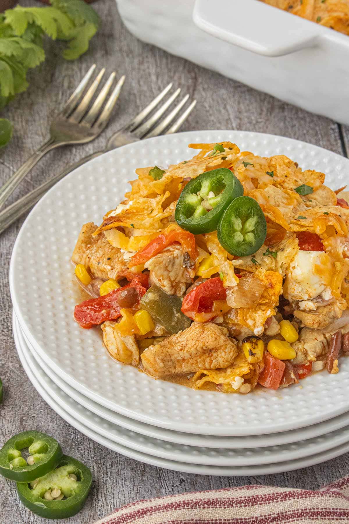 Serving of 7 layer Tex-Mex chicken casserole with chicken, peppers, beans, corn, melted cheese, and jalapeño slices on white plates.