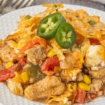 Close-up of cheesy 7 layer Tex-Mex chicken casserole topped with crunchy tortilla chips and fresh jalapeño slices.