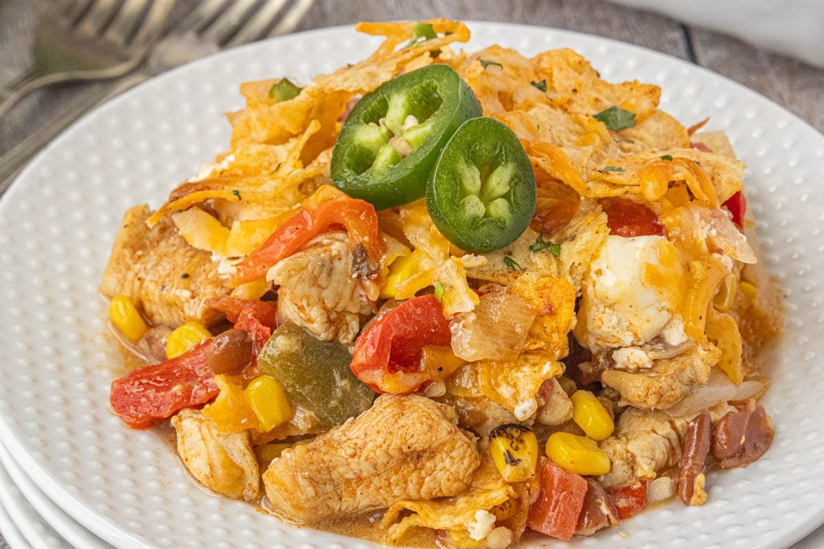 Close-up of cheesy 7 layer Tex-Mex chicken casserole topped with crunchy tortilla chips and fresh jalapeño slices.