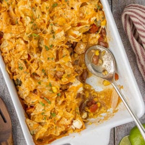 Baked 7 layer Tex-Mex chicken casserole topped with crunchy tortilla chips and melted cheese in a white casserole dish.