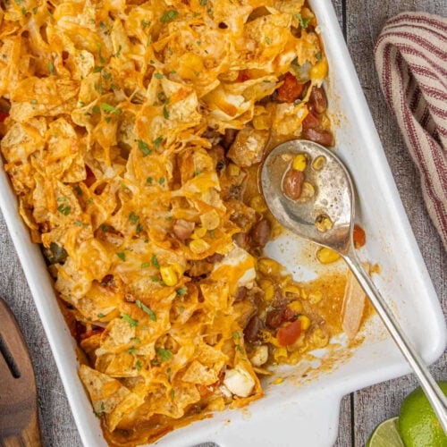 Baked 7 layer Tex-Mex chicken casserole topped with crunchy tortilla chips and melted cheese in a white casserole dish.