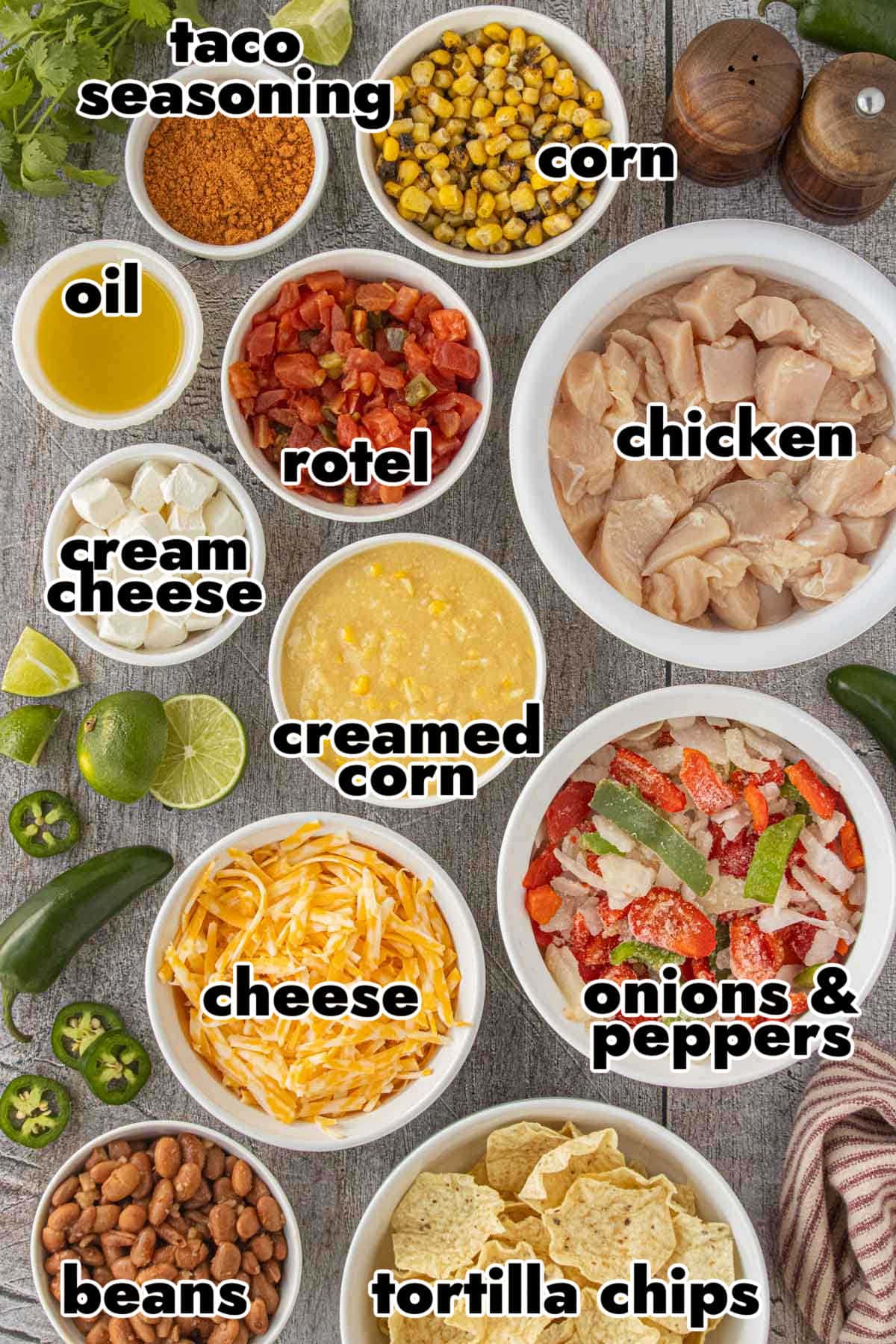 Ingredients for 7 layer Tex-Mex chicken casserole including chicken, taco seasoning, Rotel, cream cheese, corn, beans, cheese, peppers, onions, tortilla chips, and creamed corn arranged in bowls.
