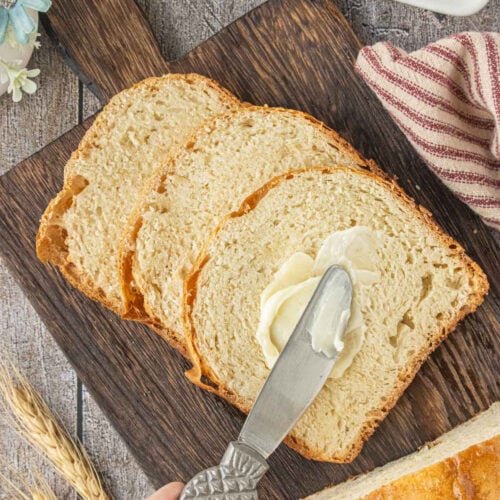 Overhead view of sliced Amish white bread with butter being spread on a slice after baking in a bread machine.