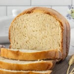 Fresh loaf of Amish white bread made in a bread machine with sliced bread on a wooden board.