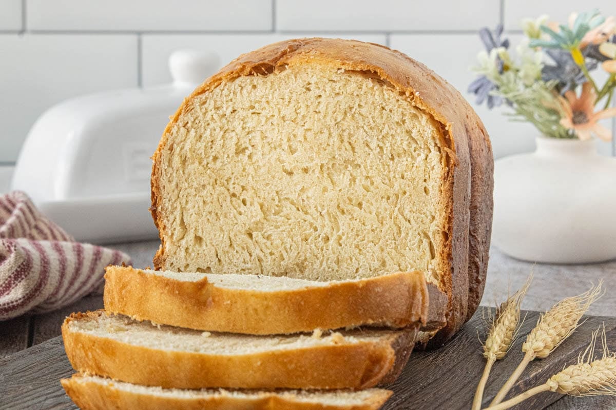 Fresh loaf of Amish white bread made in a bread machine with sliced bread on a wooden board.