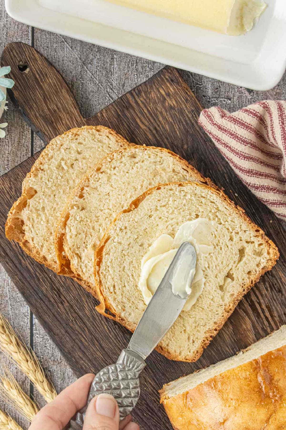 Hand spreading butter on a slice of homemade Amish white bread made in a bread machine.