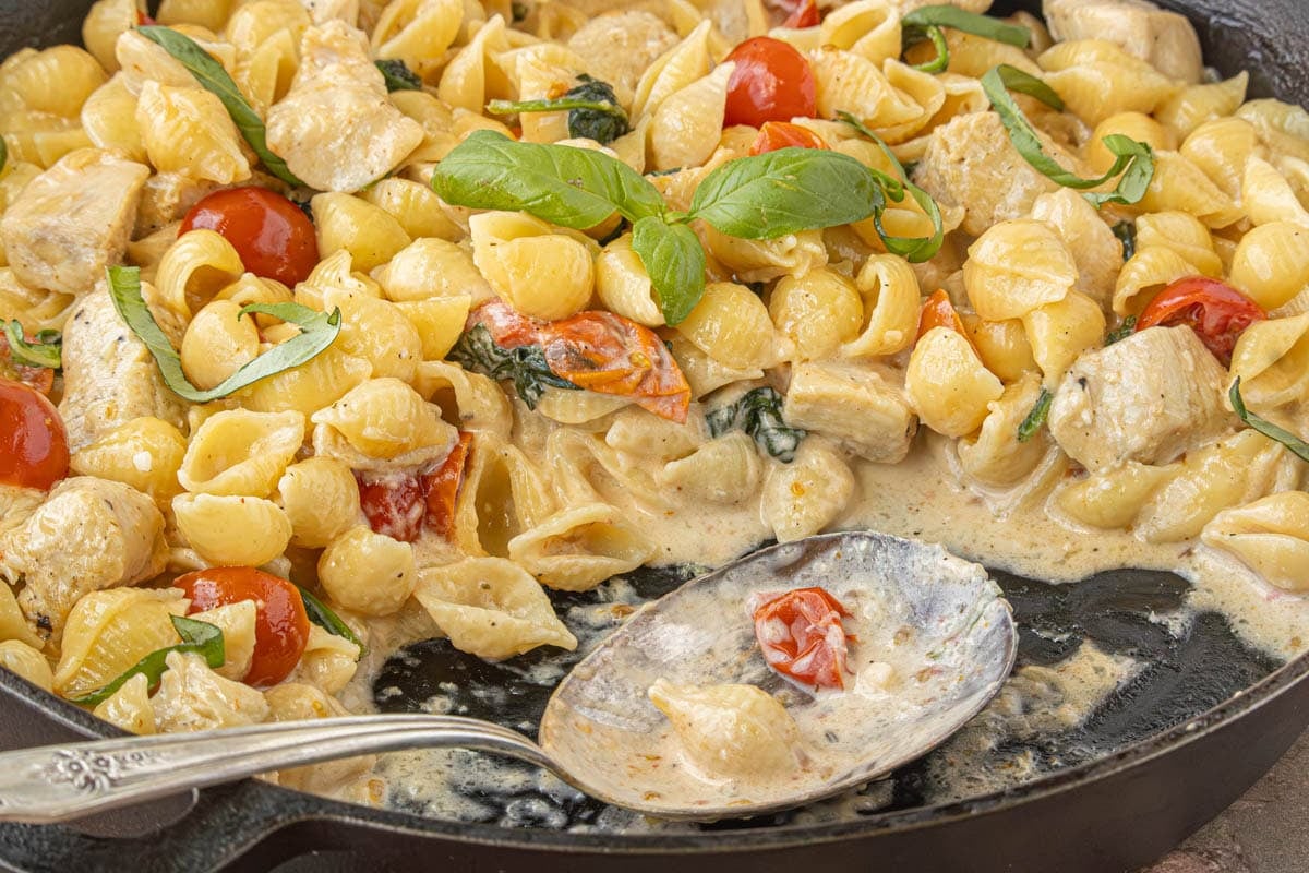 One pot chicken spinach Alfredo pasta served in a black skillet with creamy Parmesan sauce and fresh basil
