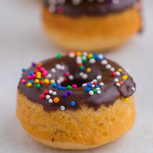 Chocolate glazed baked pancake mix donut with colorful sprinkles and stacked donuts in the background.