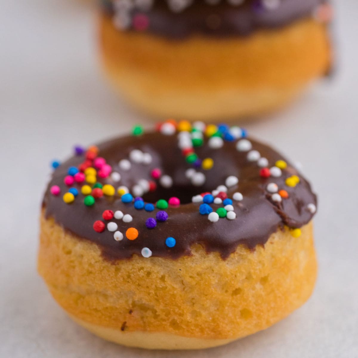 Chocolate glazed baked pancake mix donut with colorful sprinkles and stacked donuts in the background.