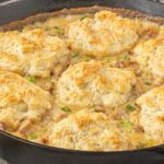 Biscuits and sausage gravy pot pie topped with golden homemade biscuits in a cast iron skillet