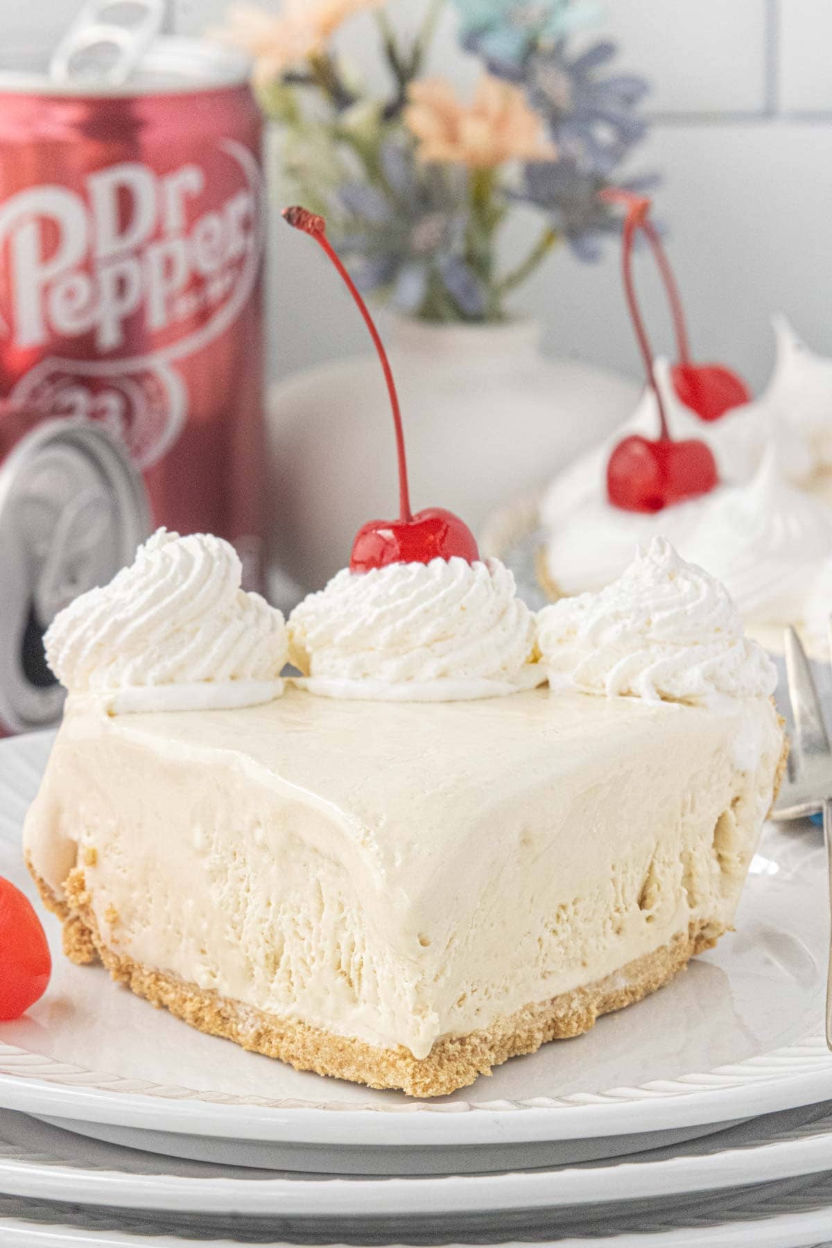 Slice of creamy Dr Pepper icebox pie topped with whipped cream and a maraschino cherry on a dessert plate.