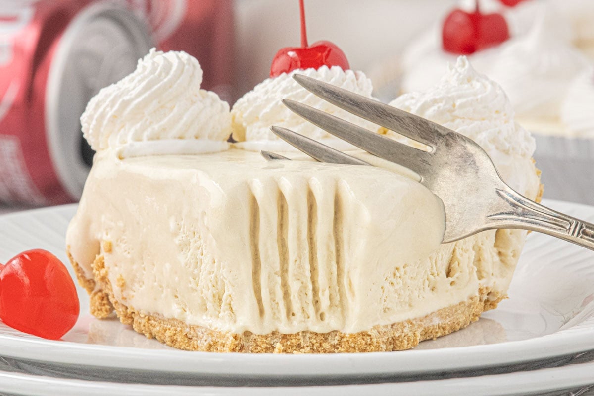 Fork cutting into a creamy slice of Dr Pepper icebox pie topped with whipped cream and cherries.