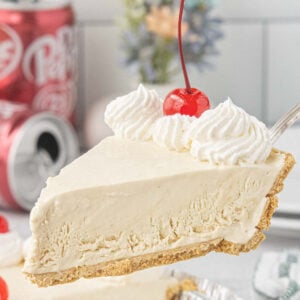 Slice of Dr Pepper icebox pie with graham cracker crust, whipped cream, and maraschino cherry lifted from the pie.
