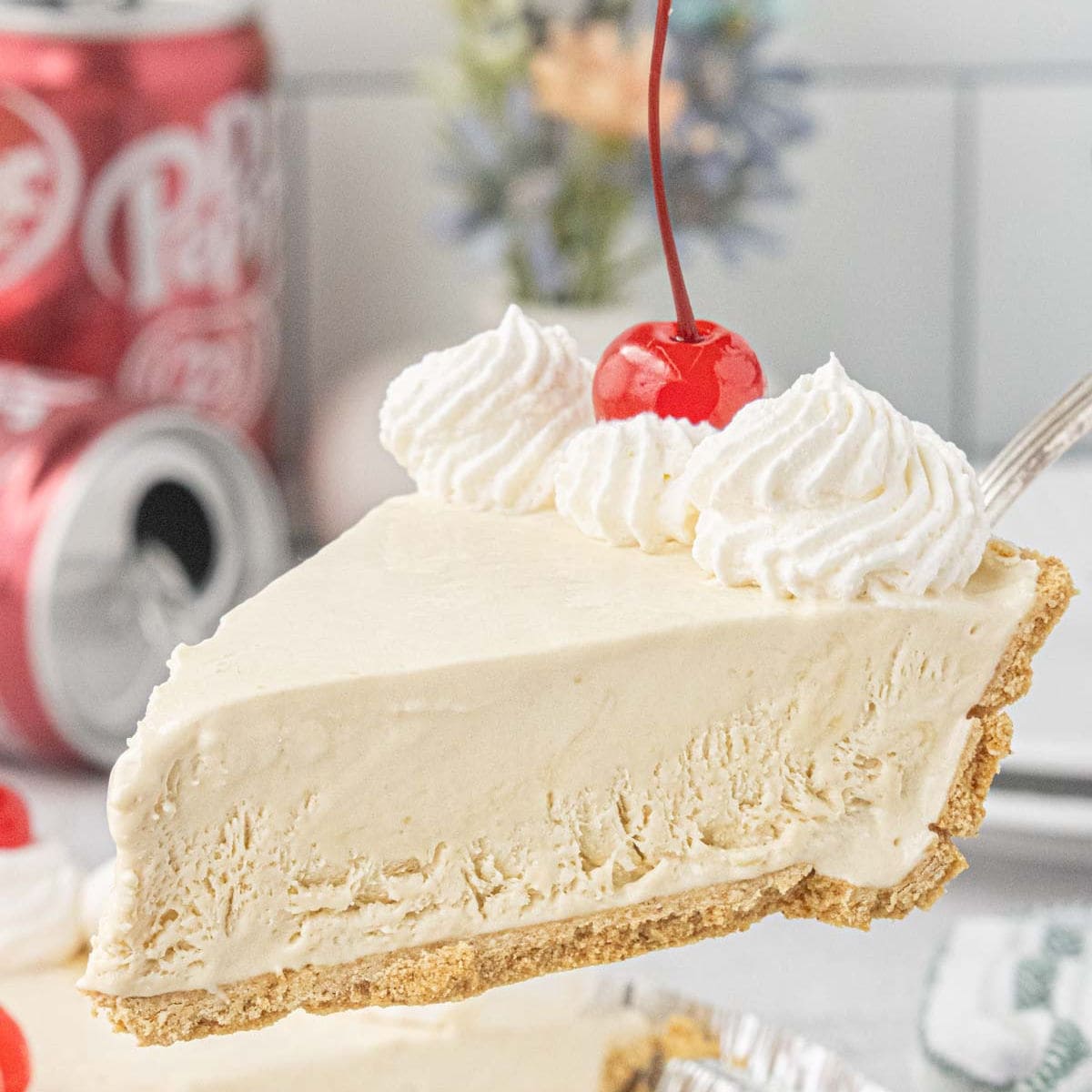 Slice of Dr Pepper icebox pie with graham cracker crust, whipped cream, and maraschino cherry lifted from the pie.