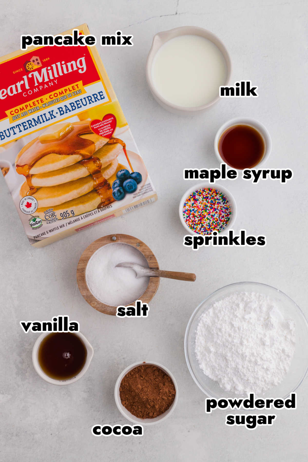 Ingredients for baked pancake mix donuts including pancake mix, milk, vanilla, cocoa powder, powdered sugar, and sprinkles.