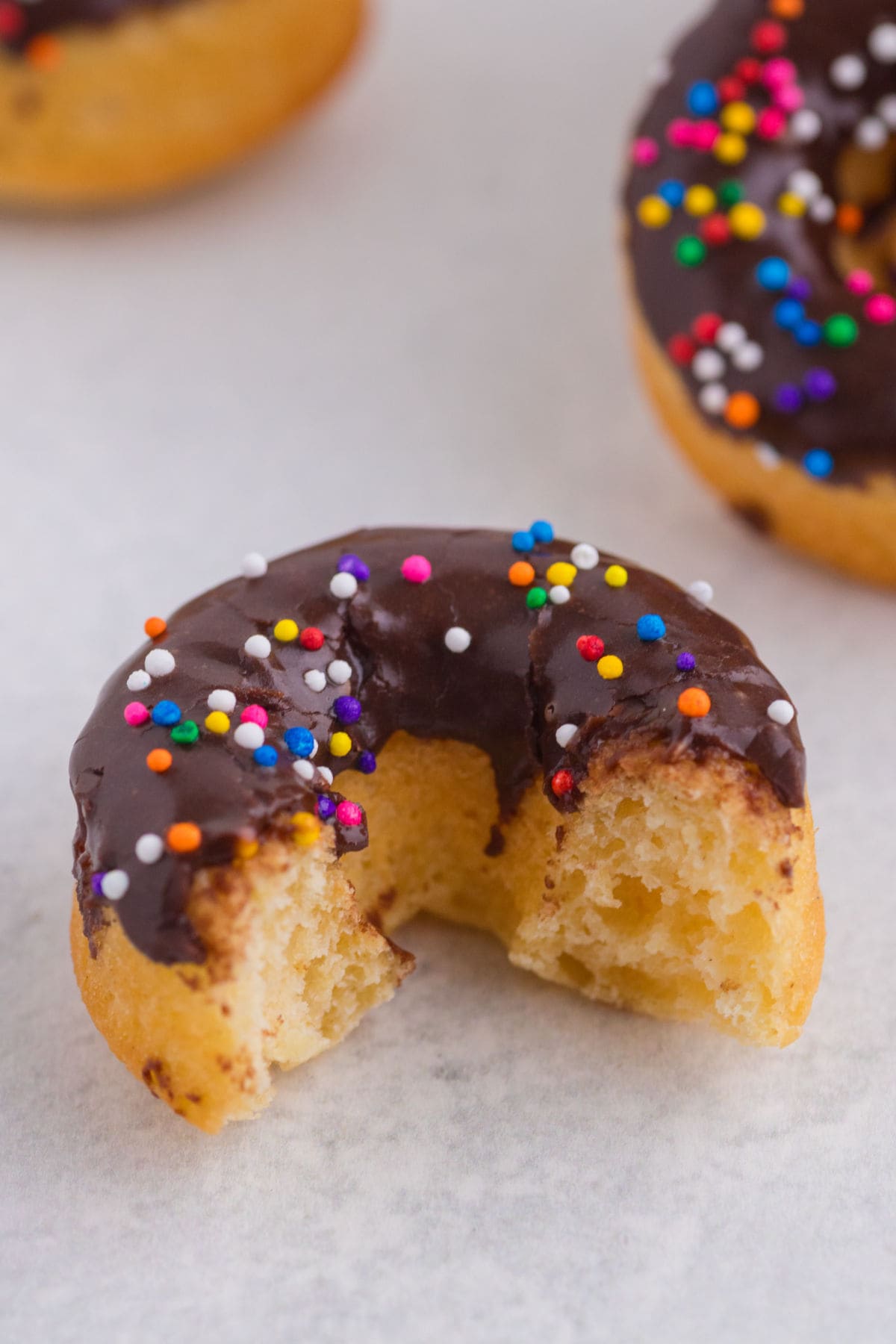 Chocolate glazed baked donut with a bite taken out showing the soft cake-like texture inside.