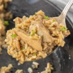 A spoonful of stick of butter chicken and rice casserole being lifted from the skillet.