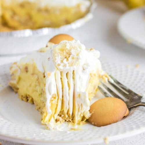A slice of banana pudding pie on a white plate with Nilla Wafers to the side.