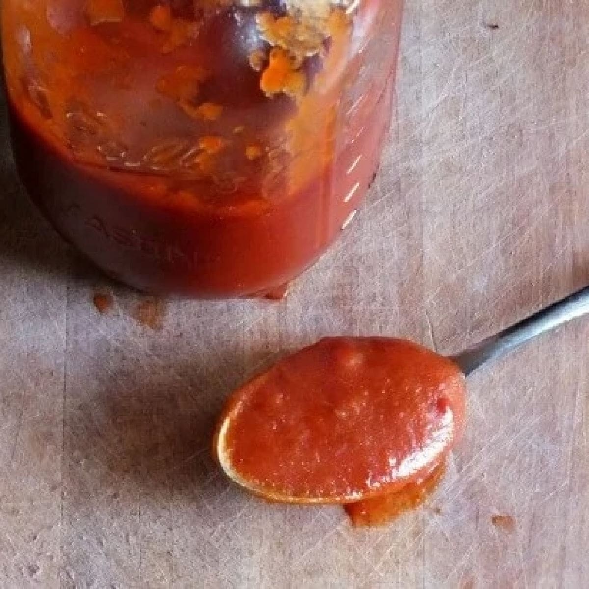 Vintage Texas bbq sauce recipe in a jar with a spoonful of sauce on the table.
