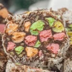 Close-up of church window cookies with colorful marshmallows, chocolate, pecans, and coconut coating stacked on a serving plate.
