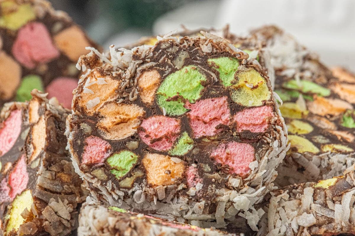 Close-up of church window cookies with colorful marshmallows, chocolate, pecans, and coconut coating stacked on a serving plate.