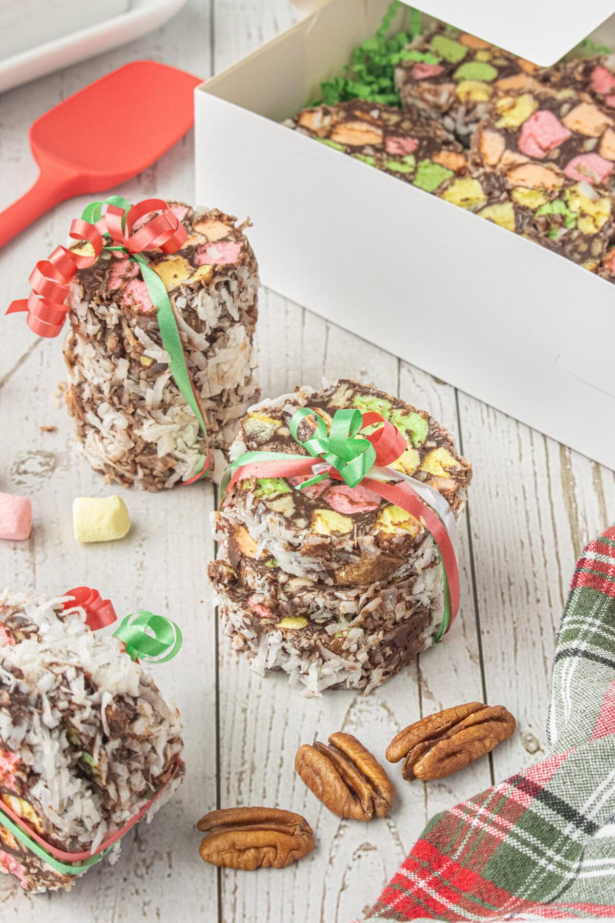 Homemade church window cookies wrapped with festive ribbon beside a gift box filled with colorful chocolate marshmallow cookies.