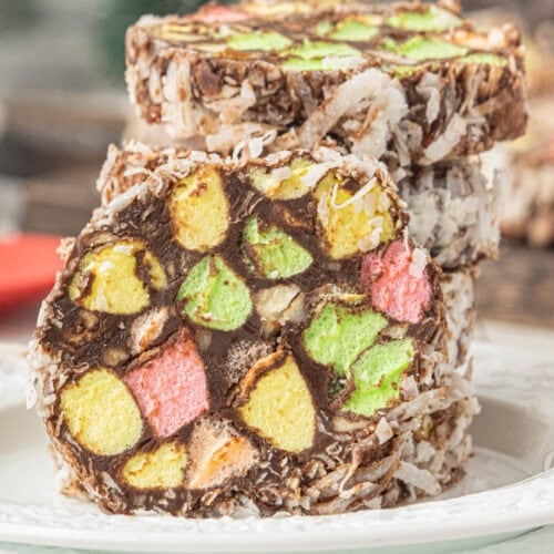Colorful church window cookies made with chocolate, pastel marshmallows, pecans, and coconut stacked on a white plate.