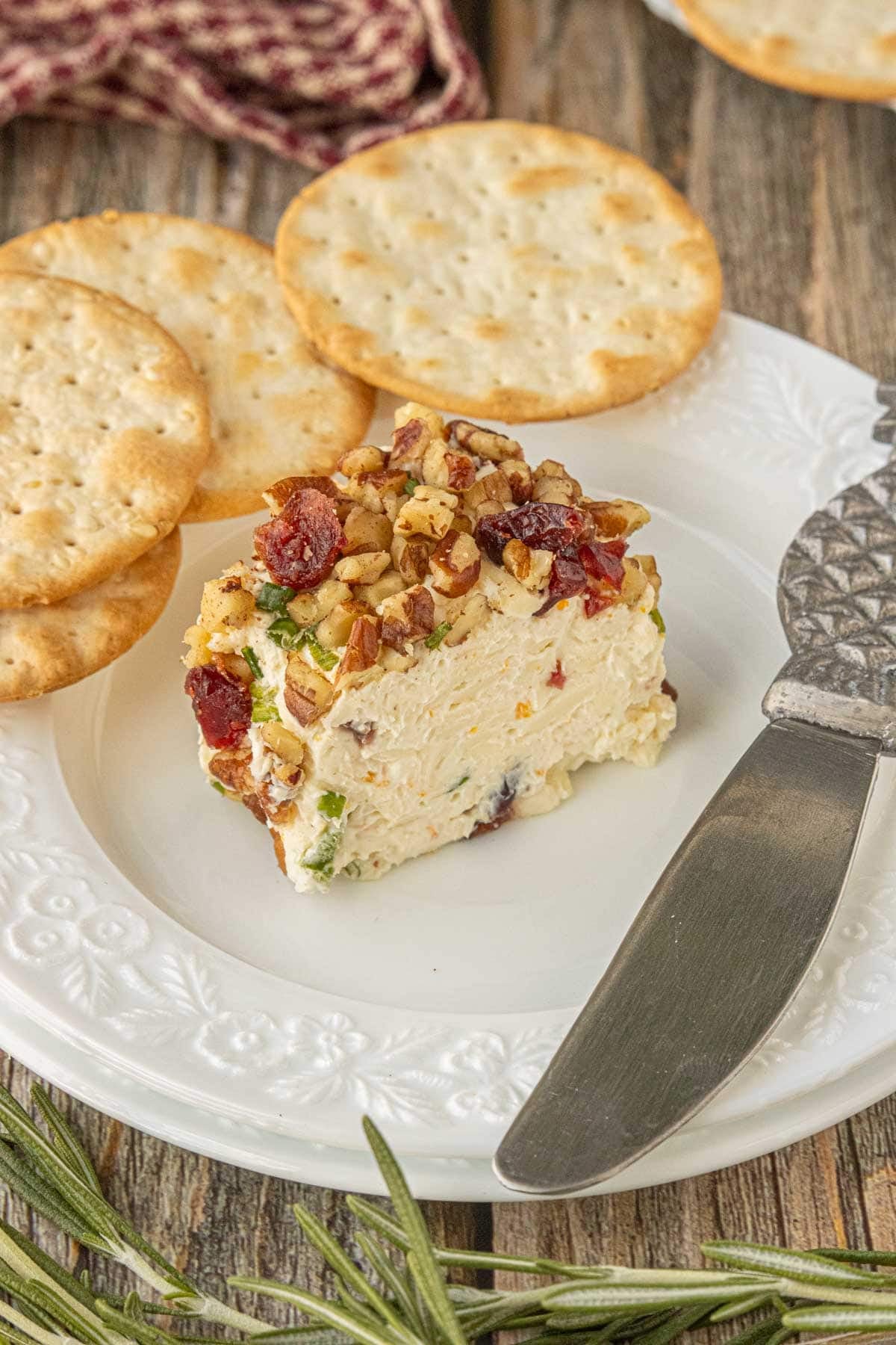 Slice of cranberry cheese ball with pecans, dried cranberries, and cheddar served with crackers.
