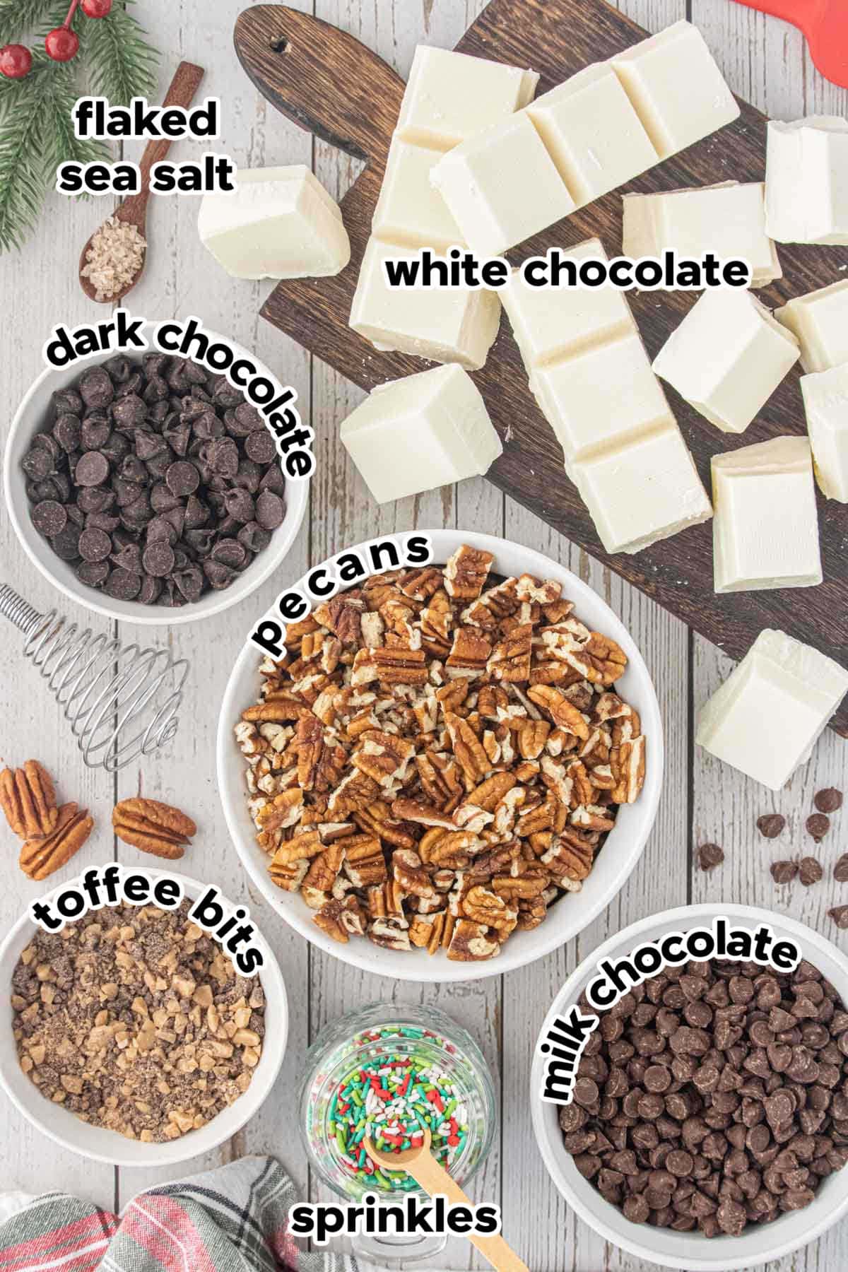Ingredients for crockpot candy including white chocolate, milk chocolate, dark chocolate, pecans, toffee bits, flaky sea salt, and Christmas sprinkles.