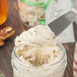 Butter knife holding a generous scoop of fluffy pecan praline honey butter above a glass jar.