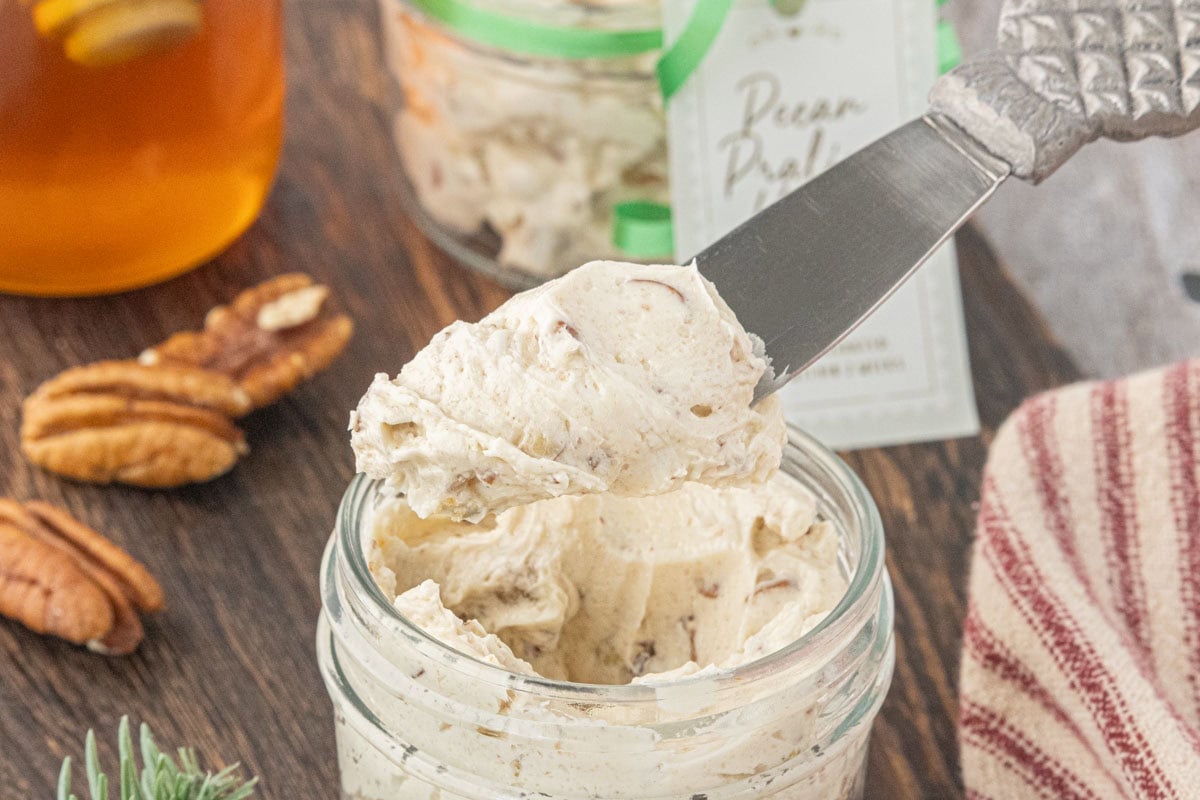 Butter knife holding a generous scoop of fluffy pecan praline honey butter above a glass jar.