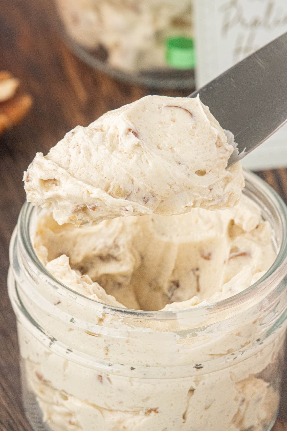 Butter knife holding a generous scoop of fluffy pecan praline honey butter above a glass jar.